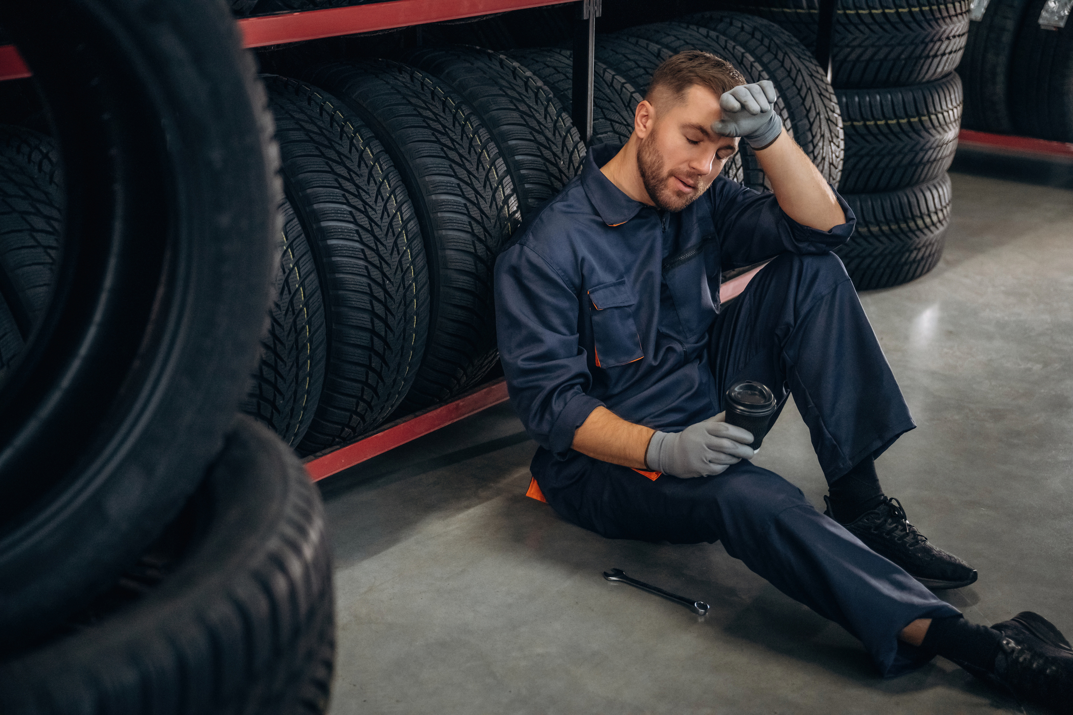 Taking a break, Male mechanic sitting on the floor in a garage against a row of tyres