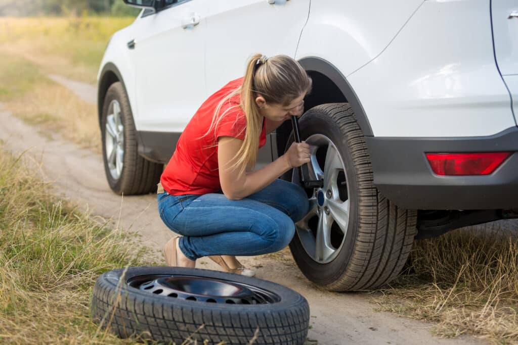 Woman unscrewing car wheel nuts to change flat tyre